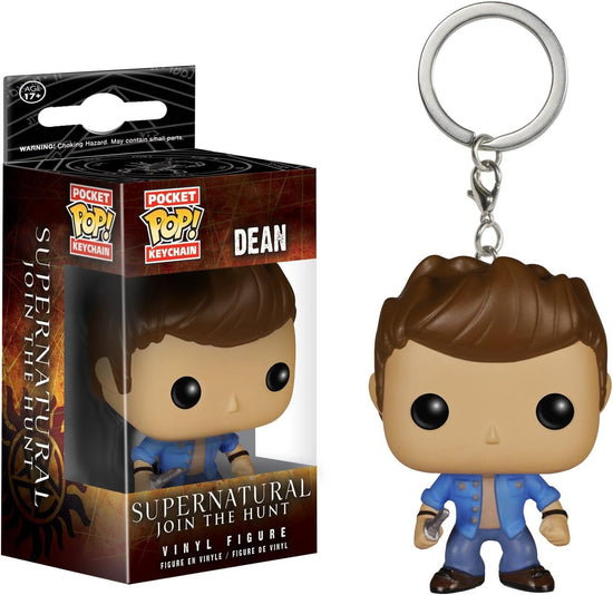 Close up of a keychain in the shape of Dean Winchester, wearing jeans and a blue shirt. His features are cartoonish, with an extra large head. Next to the keychain is a brown box containing the same keychain. At the bottom of the box is white text saying "Supernatural, Join the Hunt. Vinyl figure."