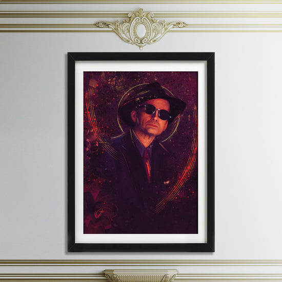 A black-framed picture on a white wall. The picture depicts the character Crowley from the TV series "Good Omens," wearing a black suit and hat and surrounded by dark red and black swirls. Above and below the framed picture is ornate crown moulding.