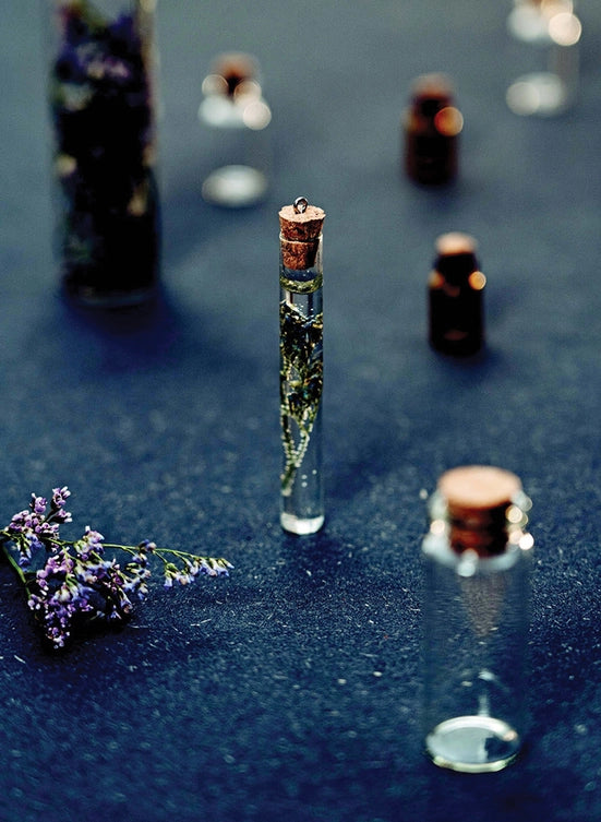 A handful of glass vials, standong on a dark blue cloth. In the vials are various ingredients for spells.