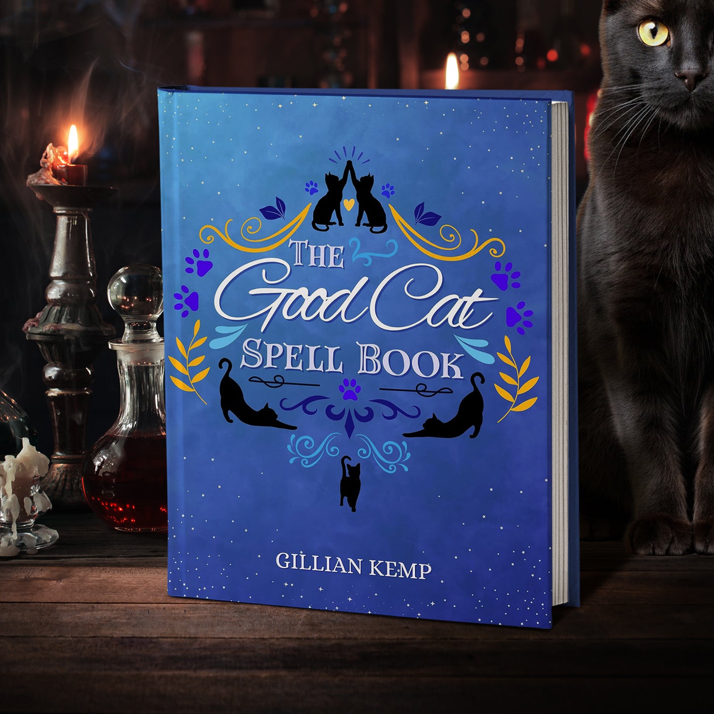 A blue hardcover book on a wooden table. The cover depicts black silhouettes of cats on a blue background. White text says "The good cat spell book." Next to the book is a black cat. In the background are candlesticks and apothecary bottles.