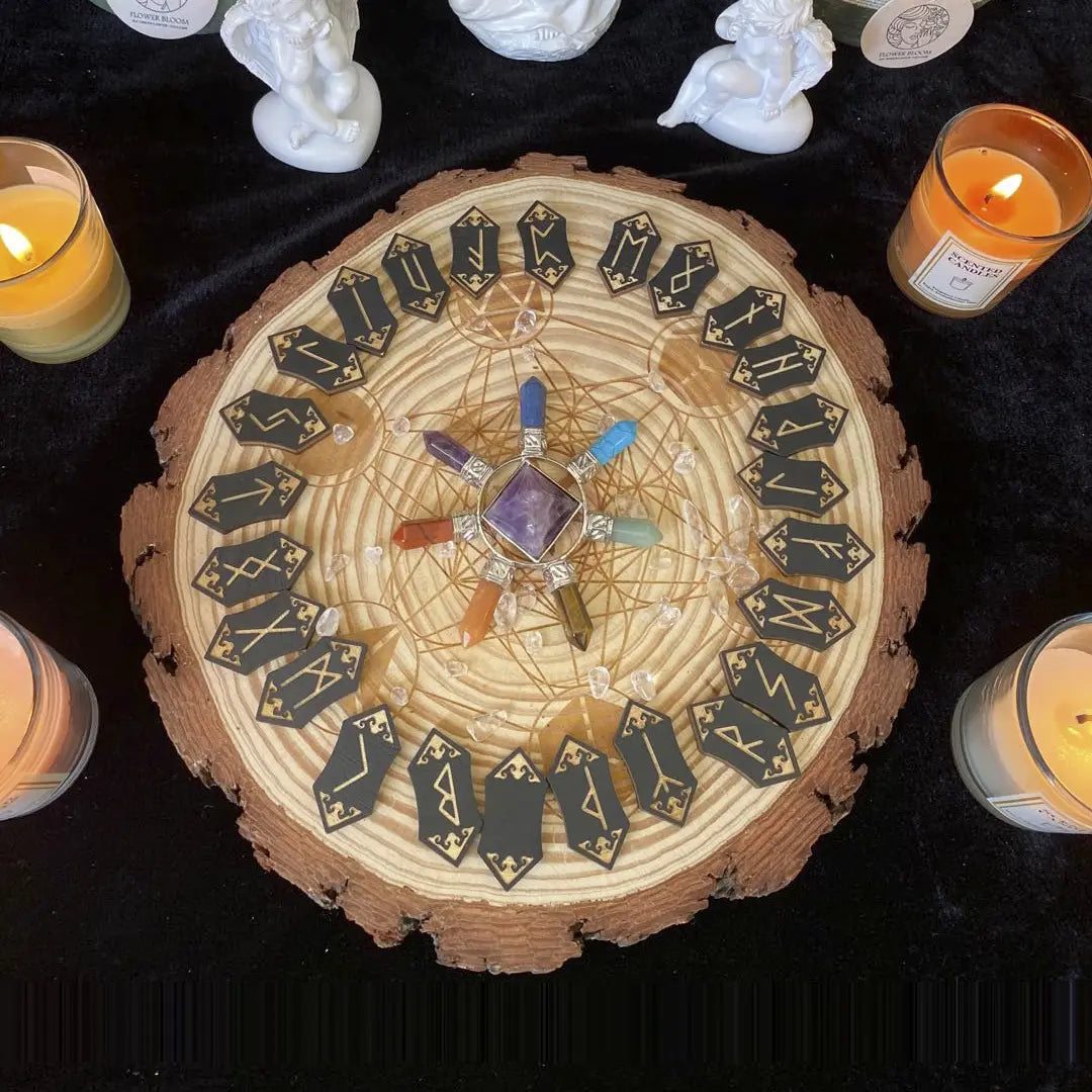 24 cards, pointed on both ends, arranged in a circle around a flat tree stump. Each card is black, with a Nordic rune printed on it in gold. In the center is a set of 7 crystals, each a different color, in a circle around a purple crystal cube. Lit candles are arranged next to the stump.