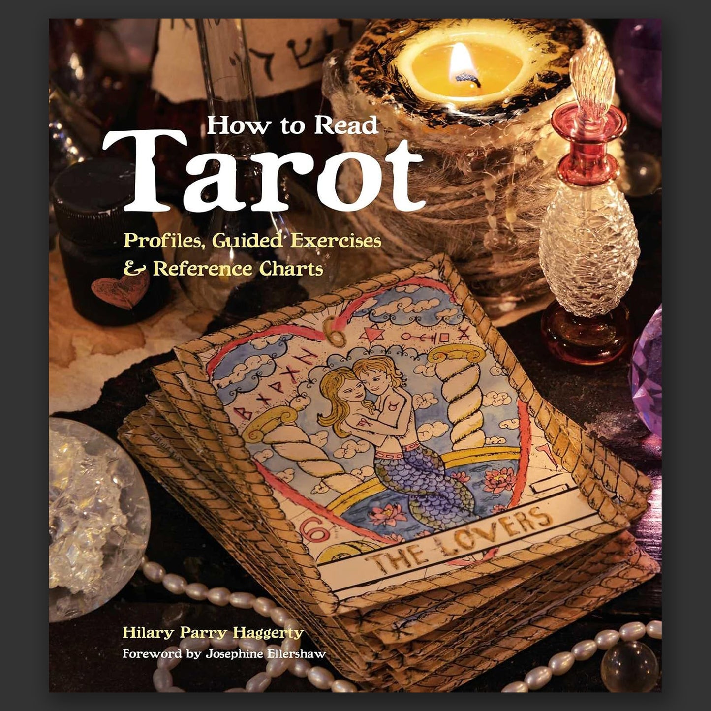 A hardcover book on a grey background. On the front are images of tarot cards, surrounded by glass jars, candles, and other trinkets often used by Tarot readers. White and yellow text says "How to read tarot. Profiles, guided exercises, and reference charts."
