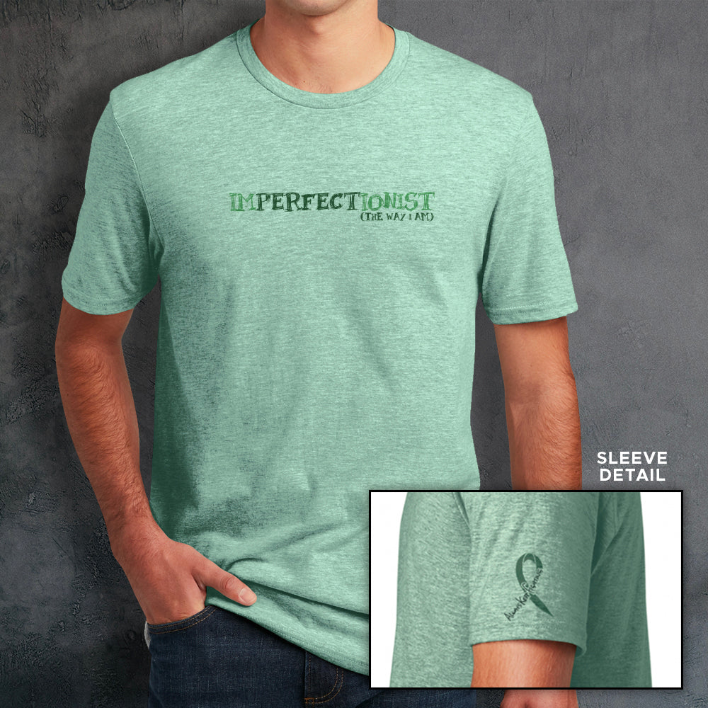 A male model wearing a mint green t-shirt. The front reads "IMPERFECTIONIST". The word "perfect" is printed in a darker shade, and the words "the way I am" are printed beneath it, so the full impression reads 'Imperfectionist / Perfect the way I am" . The sleeve bicep has a green ribbon that reads "always keep fighting" within it.