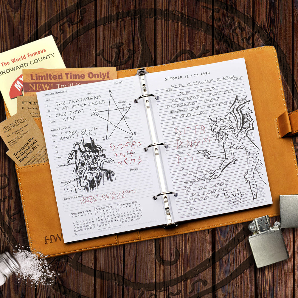 Top view of a brown faux leather journal, open against a wooden table. Spread through the center is a stack of white paper, with descriptions and drawings of demons and other monsters. Behind the paper on the left is a pocket filled with newspaper articles and advertisements. Next to the journal are a cigarette lighter and a glass bottle spilling salt onto the table.