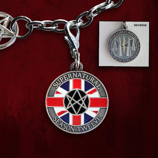A brass coin charm. The front reads "Supernatural season twelve" and shows the British men of letters symbol in front of a British flag. The back reads "I kinda always wanted to punch the devil in the face" and depicts an orange rift/portal in a grey-blue background.