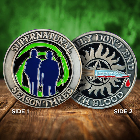 A brass coin with "Supernatural season three", a green "Mystery Spot" swirl, and 2 male sillhouettes on one side and "Family Don't End With Blood" with a knife and anti-possession symbol on the other