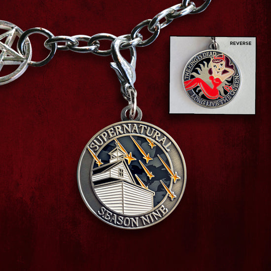 A brass charm with "Supernatural season nine", a church with falling stars on one side, and "The king is dead, long live the queen.", and a woman in a red jumpsuit with devil horns and a devil tail  with an anti-possession symbol background on the other