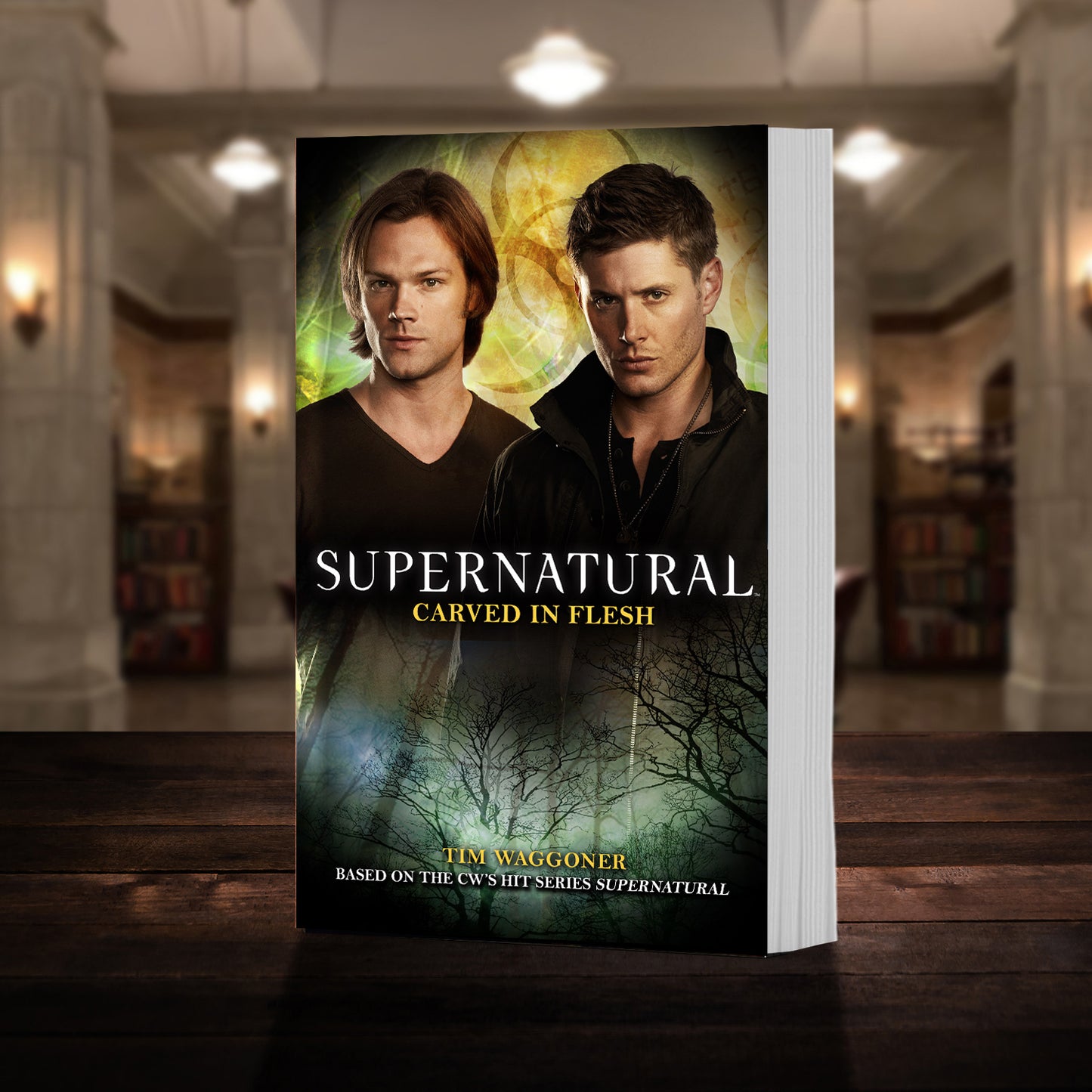 A copy of the book "Supernatural: Carved in Flesh" pictured in the "bunker" from Supernatural. The cover shows mid-season Sam and Dean Winchester and reads "Tim Waggoner - Supernatural Carved in Flesh - Based on the hit CW series SUPERNATURAL”