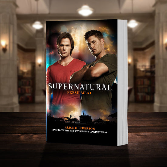 A copy of the book "Supernatural: Fresh Meat" pictured in the "bunker" from Supernatural. The cover shows mid-season Sam and Dean Winchester and reads "Alice Henderson - Supernatural Fresh Meat - Based on the hit CW series SUPERNATURAL”