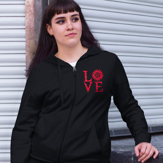 A female model wearing a black zip hoodie sweatshirt with red lettering that stacks LOVE - the "o" is the anti-possession symbol.