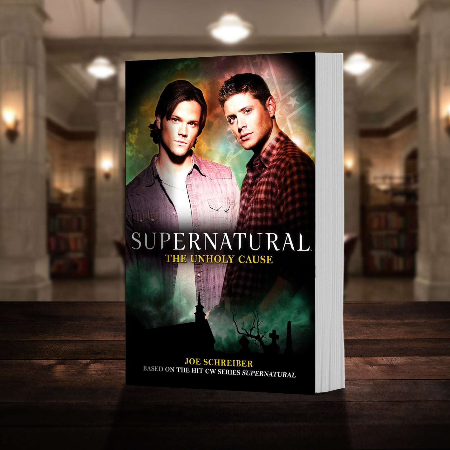 A copy of the book "Supernatural: The Unholy Cause" pictured in the "bunker" from Supernatural. The cover shows early-season Sam and Dean Winchester and reads "Supernatural The Unholy Cause - Based on the hit CW series SUPERNATURAL by Joe Schreiber”