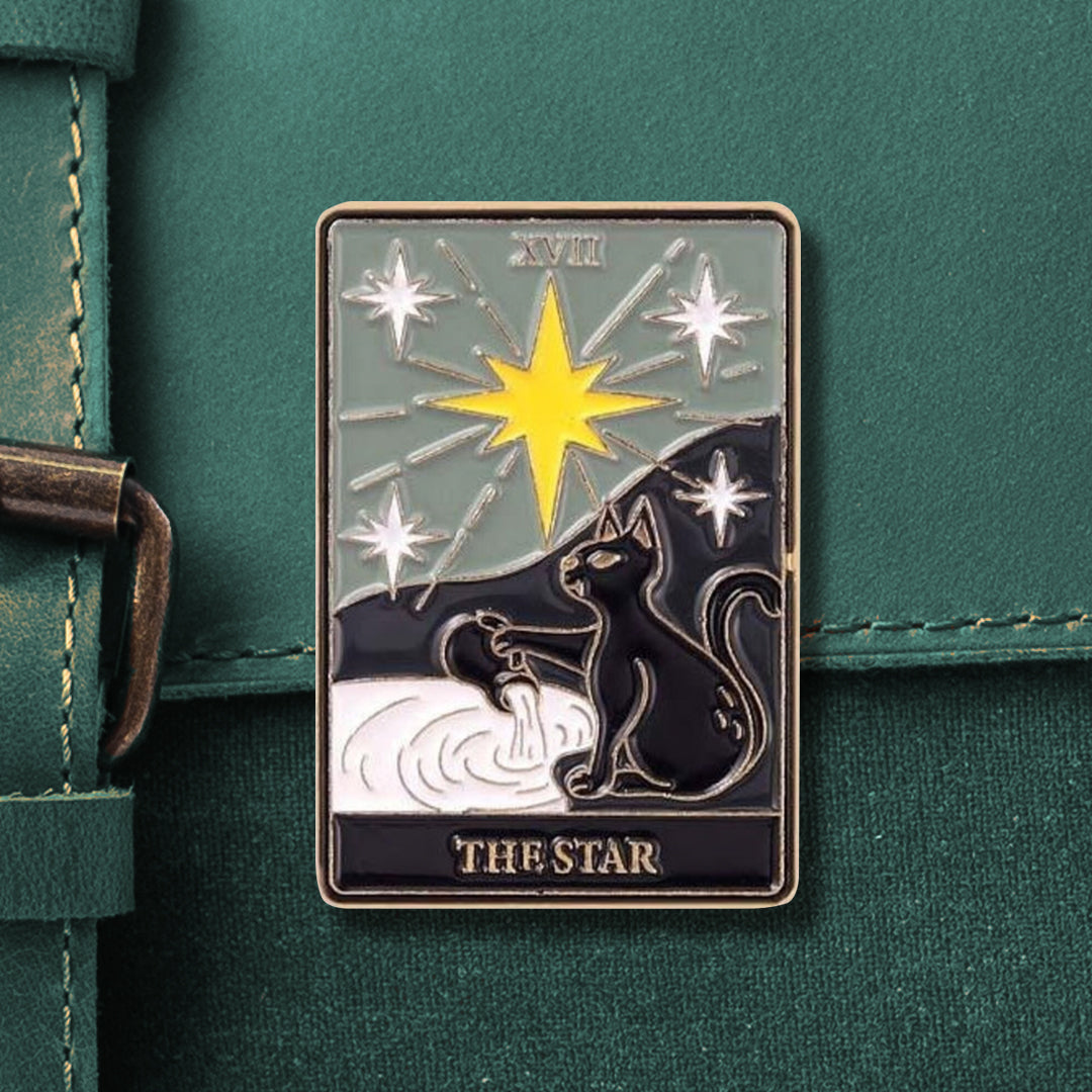A rectangular tarot pin that reads "XVII" on top and "THE STAR" on the bottom. The pin depicts a black cat spilling out a vase into a pool of white liquid, beneath a large, yellow star and 4 smaller white stars.