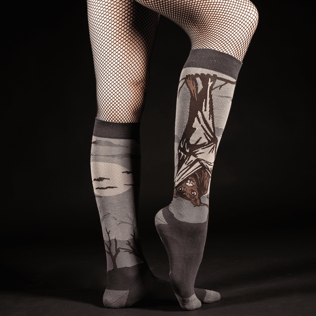 Knee-high socks with bat design worn by a person on a black background