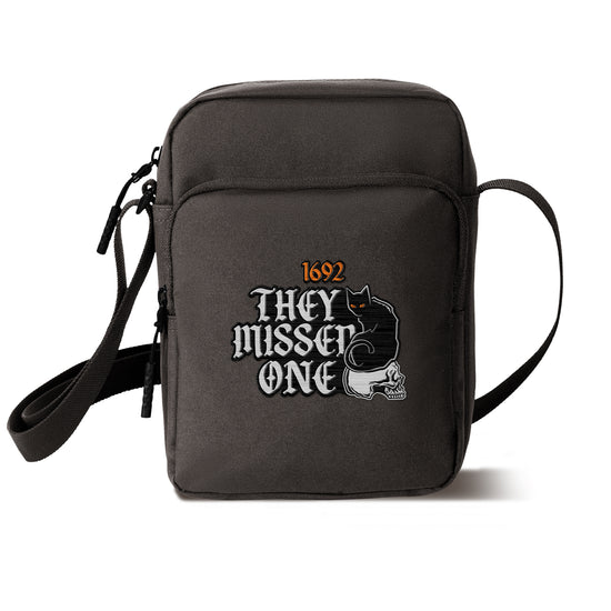 Load image into Gallery viewer, A charcoal cross body bag on a white background. On the bag is orange and white text saying &amp;quot;1692: they missed one.&amp;quot; Next to the text is an embroidered black cat with orange eyes, sitting on a white skull.
