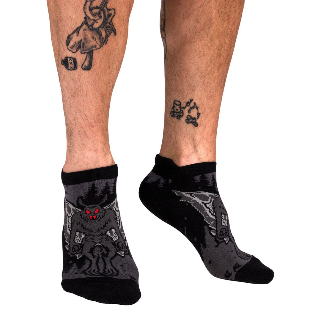 Black and gray patterned socks worn by a person with tattoos on a white background