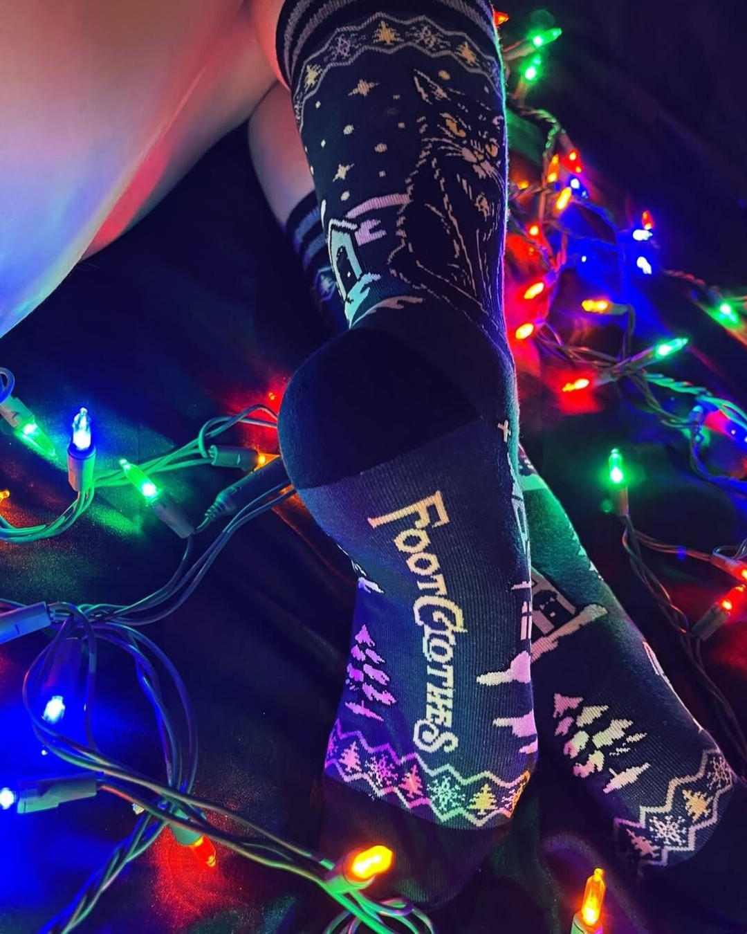 Decorative socks with 'FootGloves' branding against a colorful string light background