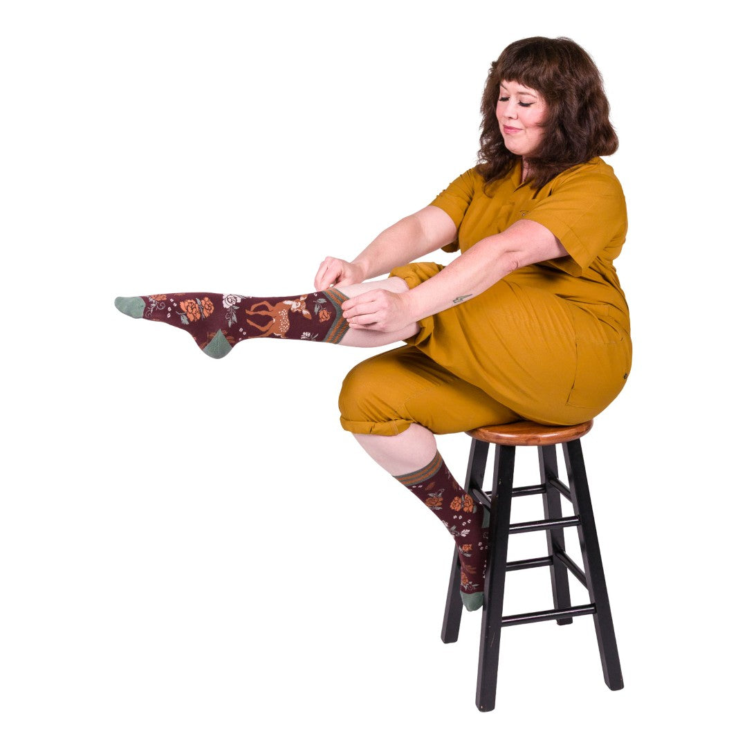 Woman sitting on a stool wearing mustard yellow outfit and patterned socks.