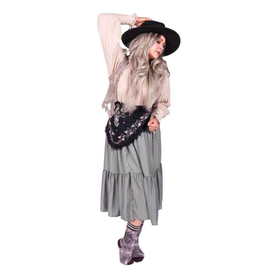 Person wearing a long gray dress, black hat, and patterned socks on a white background