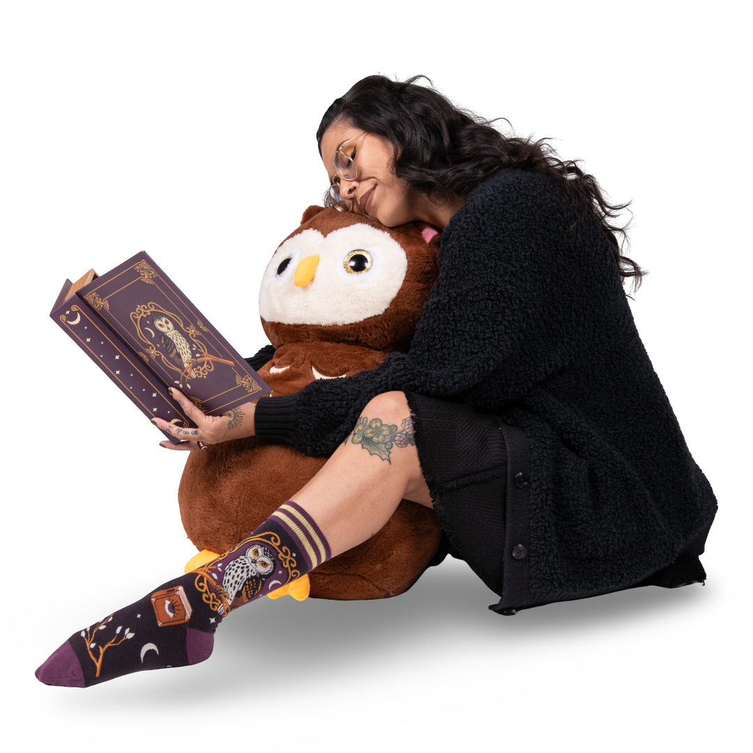 Person sitting with a large plush owl, holding a book, wearing matching socks.