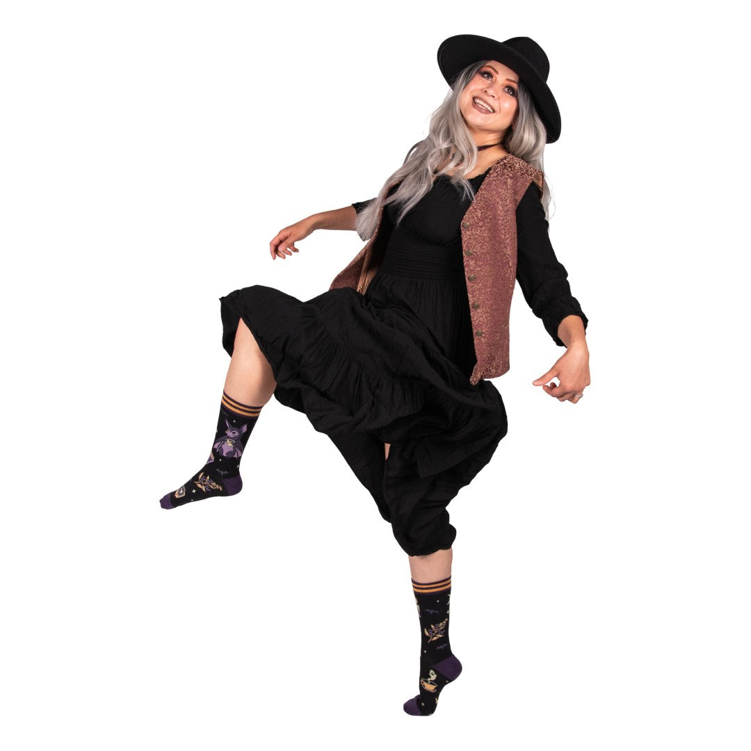 Person wearing a black dress, hat, and patterned socks on a white background