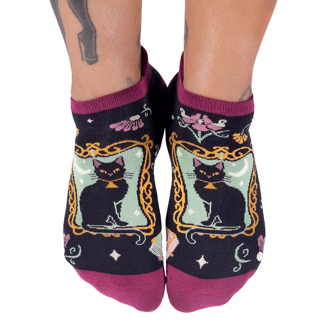 Black socks with cat designs and purple accents worn by a person on a white background