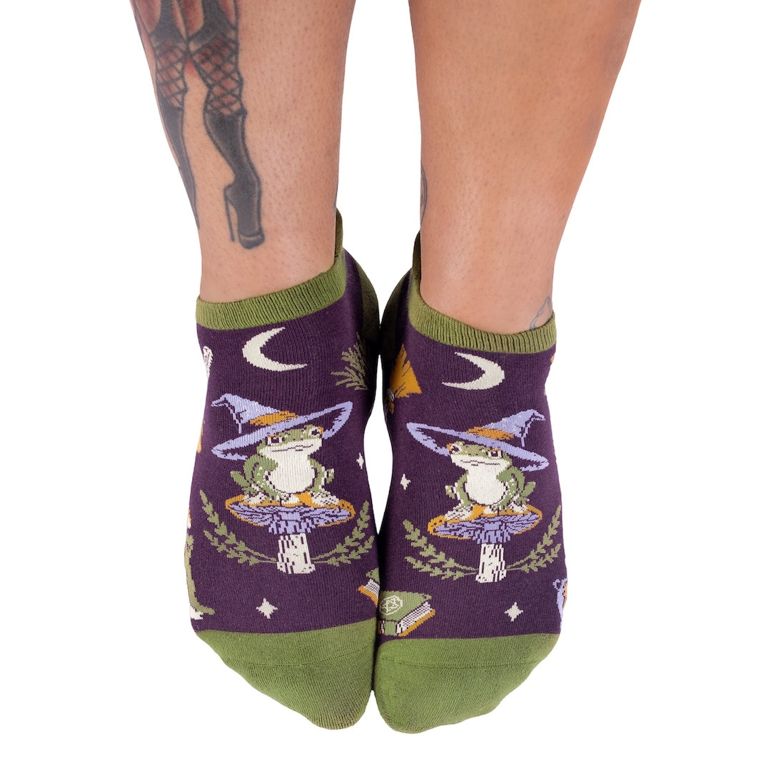 Purple socks with a frog wearing a witch hat design on a white background