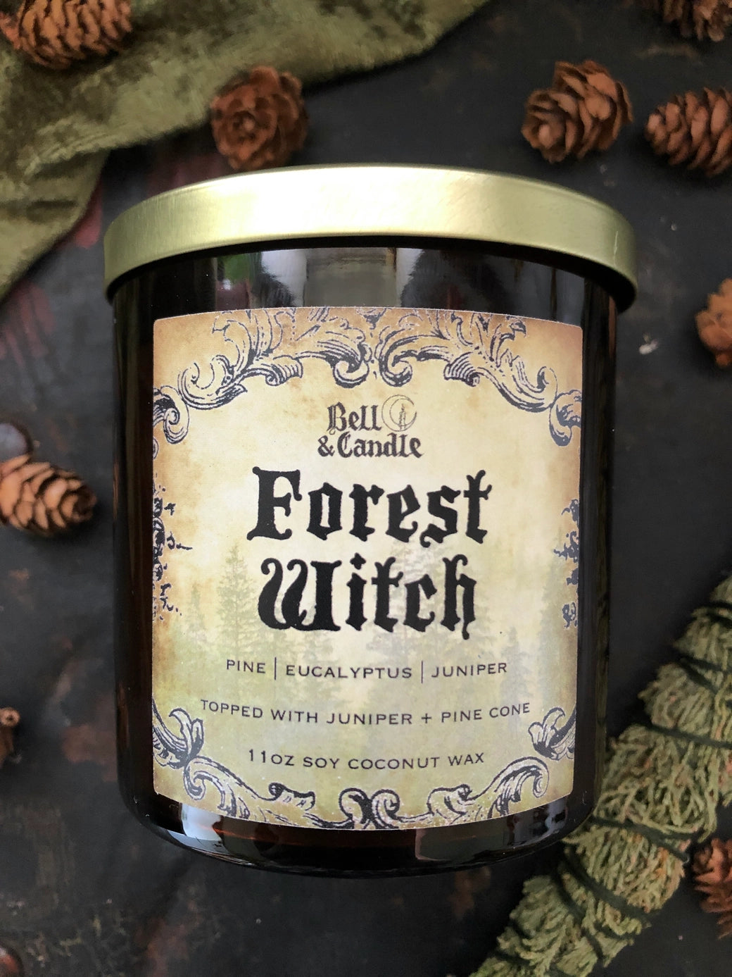 Candle jar labeled 'Forest Witch' with decorative label and pinecones surrounding it