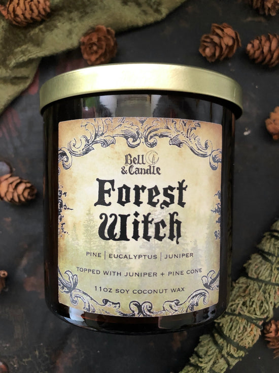 Candle jar labeled 'Forest Witch' with decorative label and pinecones surrounding it