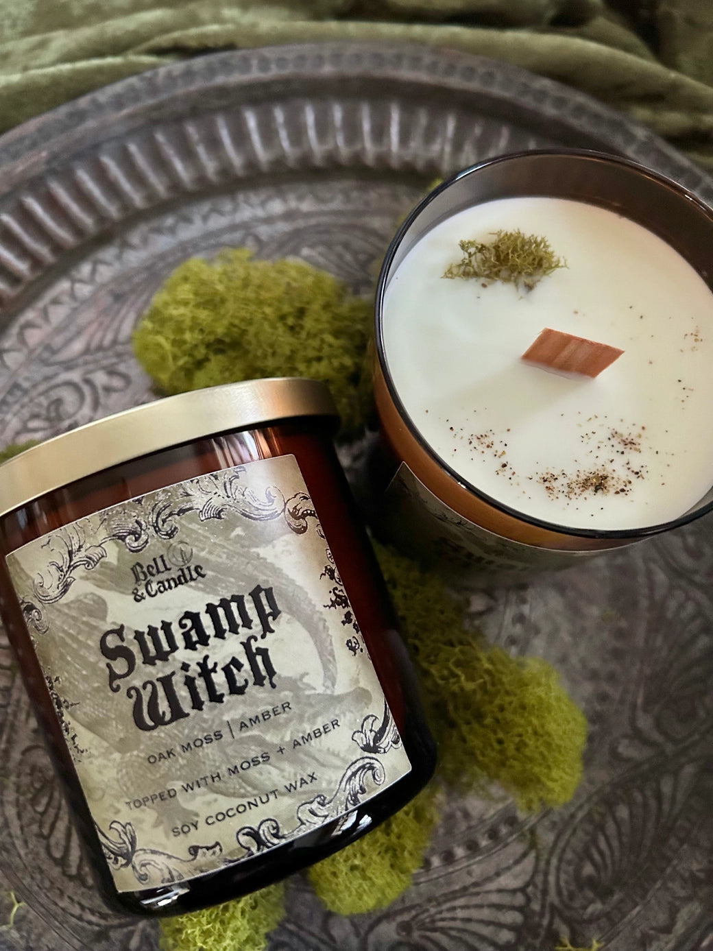 Scented candle labeled 'Swamp Witch' on a textured surface with green moss-like material.