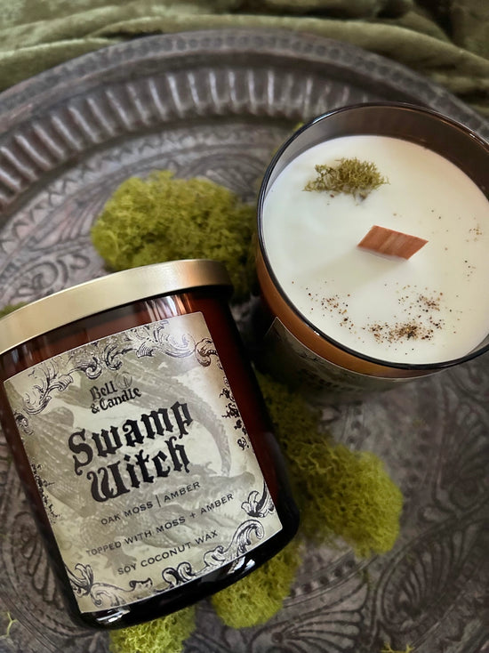 Scented candle labeled 'Swamp Witch' on a textured surface with green moss-like material.
