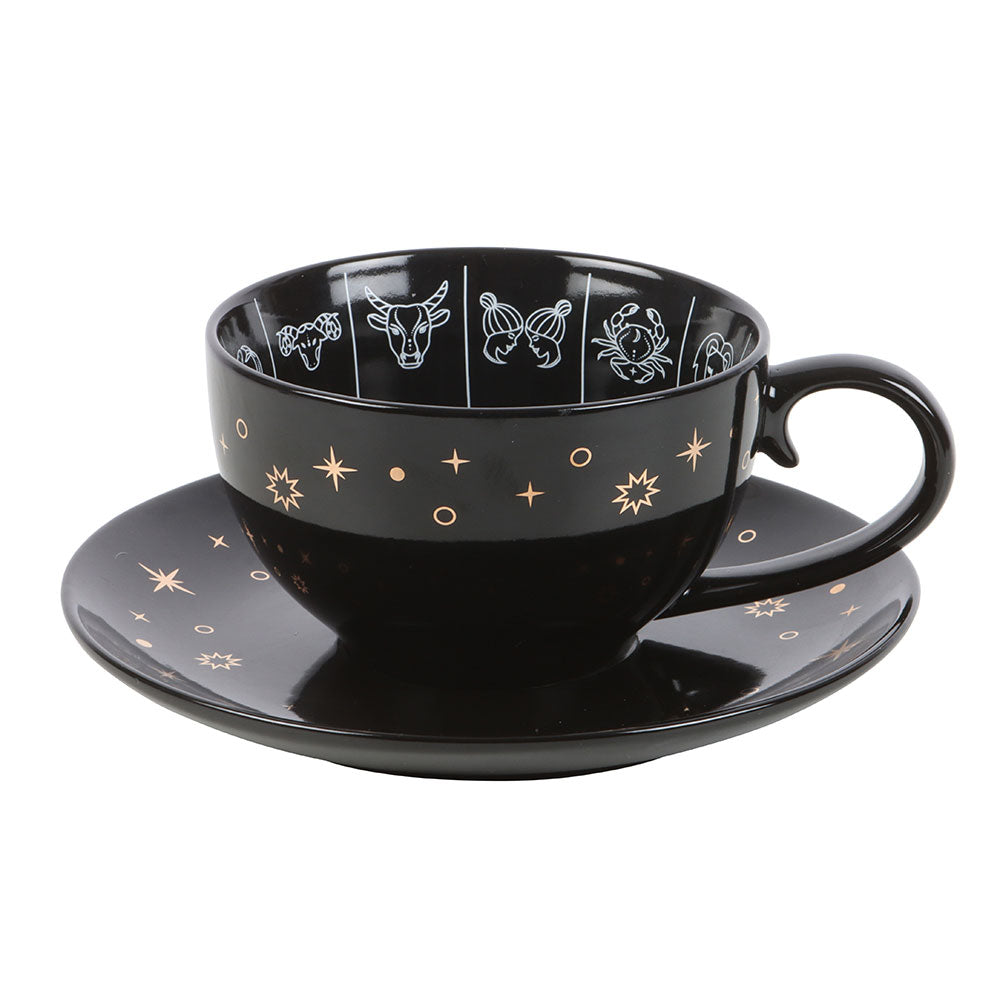 Black cup and saucer set with star and zodiac constellation designs on a white background