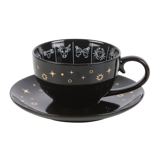 Black cup and saucer set with star and zodiac constellation designs on a white background