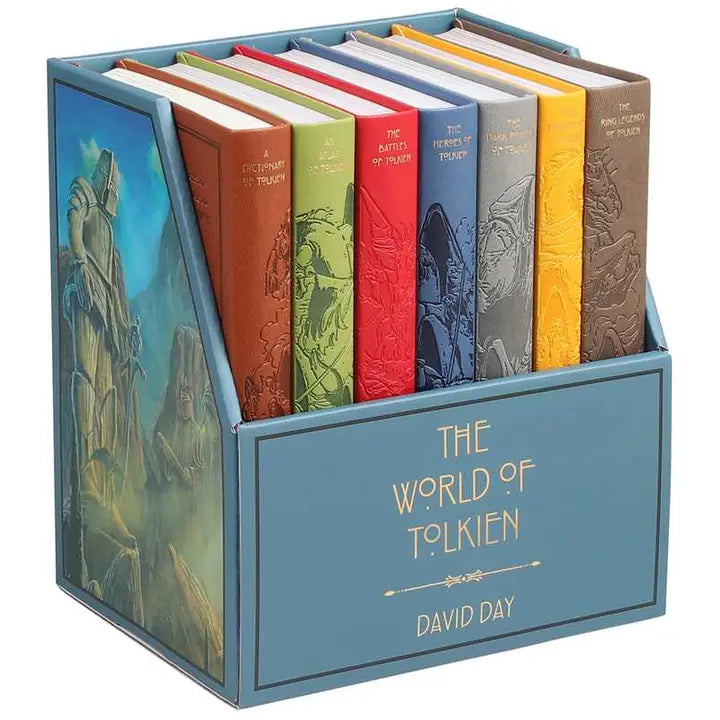 Seven hardcover books lined up side by side with their spines visible. Each book is a different color, with a drawing of creatures from the Lord of the Rings series spanning all seven books. The books are in a blue container with "The world of Tolkien" on the front in gold text. On the side of the box is a drawing of giant statues carved into cliffs.