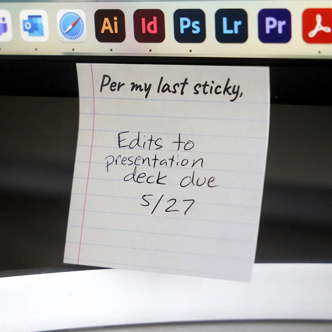 A yellow sticky note with blue horizontal lines. At the top is black text saying "per my last sticky. Handwritten text says "edits to presentation deck due 5/27." The note is affixed to a computer screen.