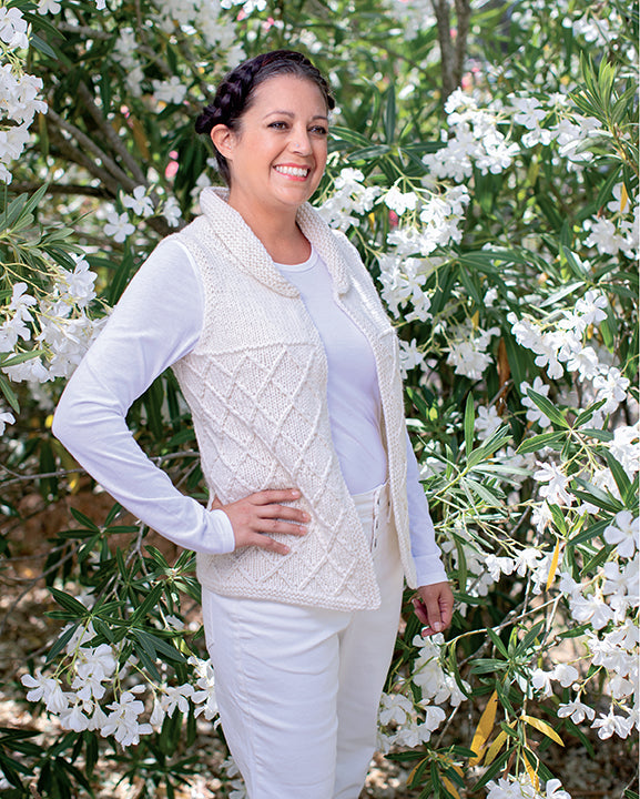 Woman wearing a white knit vest standing among white flowers and green foliage