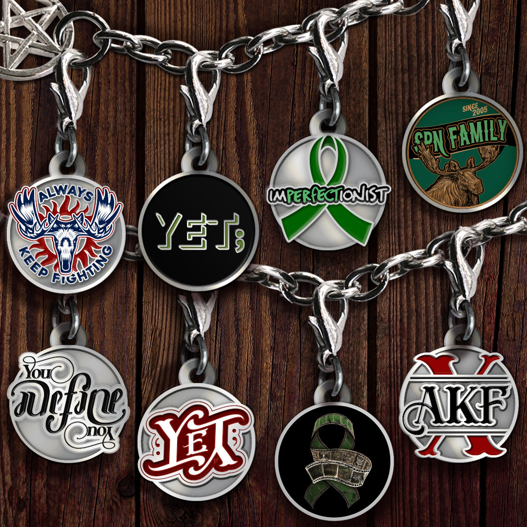 A set of silver metal charms with round charms featuring various AKF designs, displayed on a dark wood background.