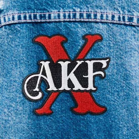 Close up of a red, black, and white iron on patch. The patch depicts the letters AKF in white, with a large red X behind them.