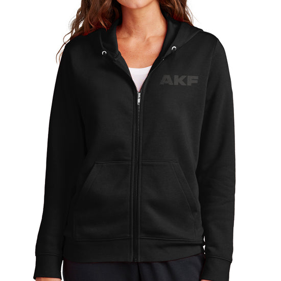 A female model wearing a black zip hoodie with the letters AKF in dark grey on the left side.