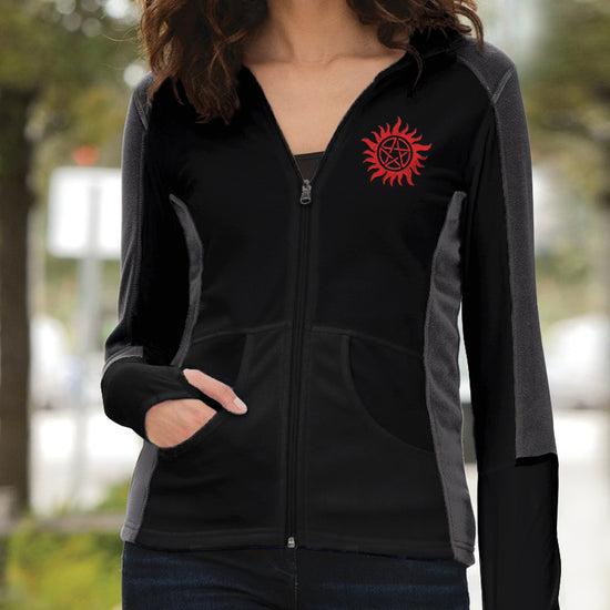 Load image into Gallery viewer, A female model wearing a black and gray fleece jacket. On the left lapel is a red anti-possession symbol. Behind the model is a city street.
