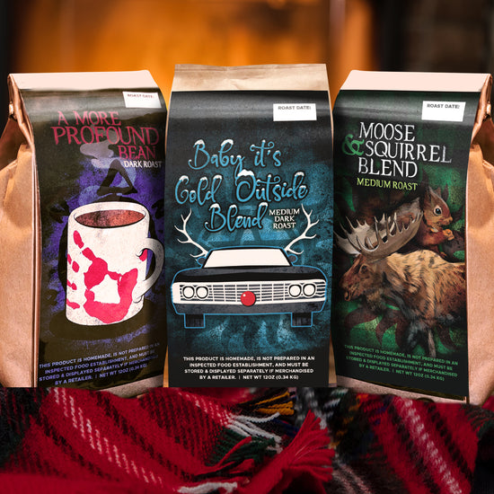 Three coffee bags with Supernatural-themed designs on a red blanket