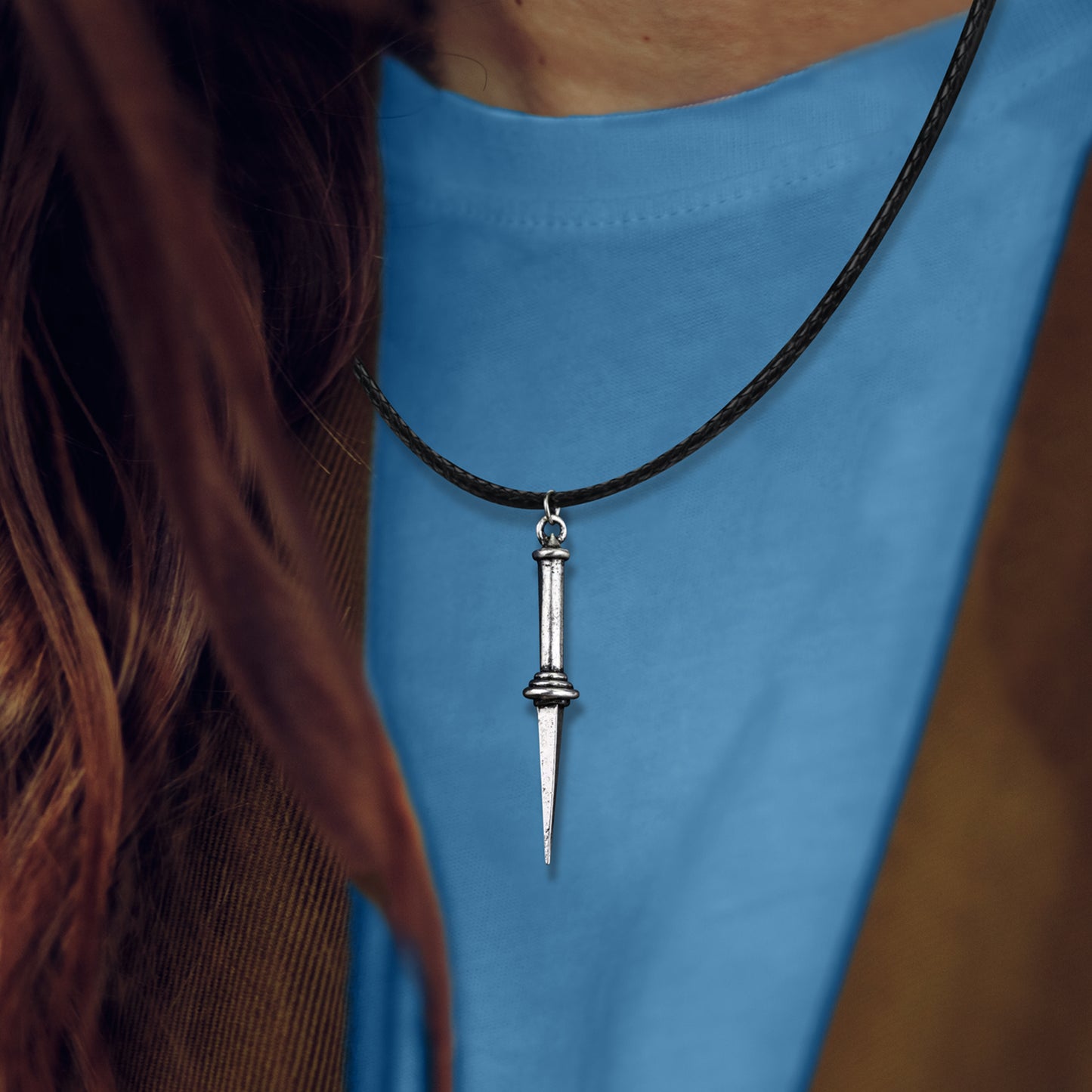Close up of a necklace pendant against a model's blue shirt. The pendant is in the shape of triple-edge Angel Blade. A black leather cord is attached to the hilt.