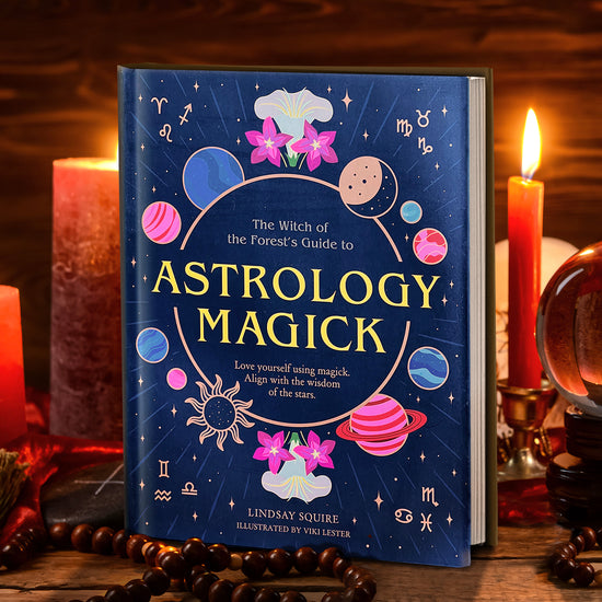 A hardcover cover of "The Witch of the Forest's Guide to Astrology Magick: Love yourself using magick, align with the wisdom of the stars". The cover is royal blue with blue and pink suns and planets.