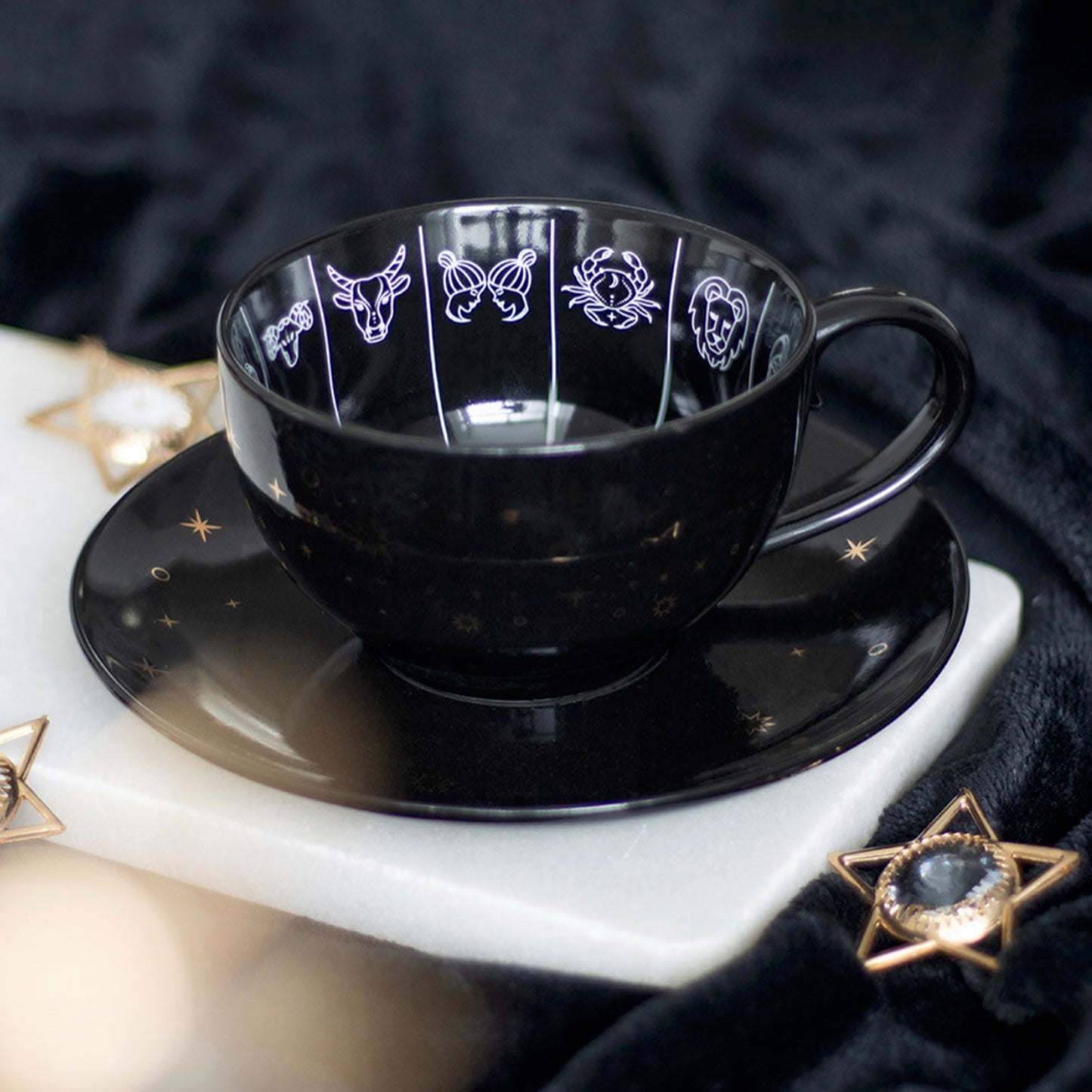 Black cup and saucer set with star and moon designs on a marble surface.