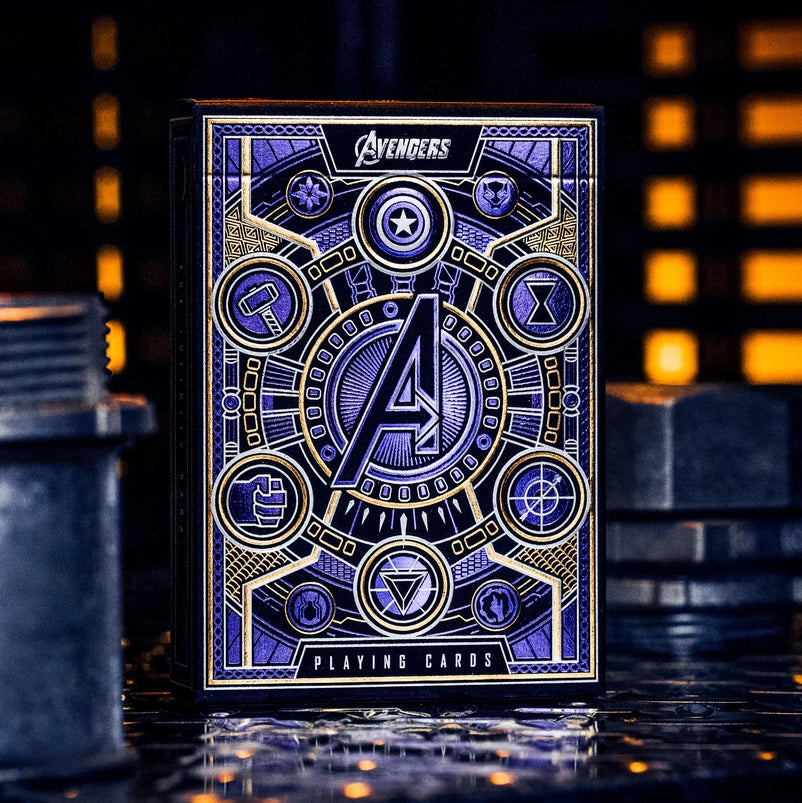 A blue and silver box of playing cards on a metal surface. The box depicts icons from the Avengers movie franchise. In the background are glowing orange lights in a metal wall.