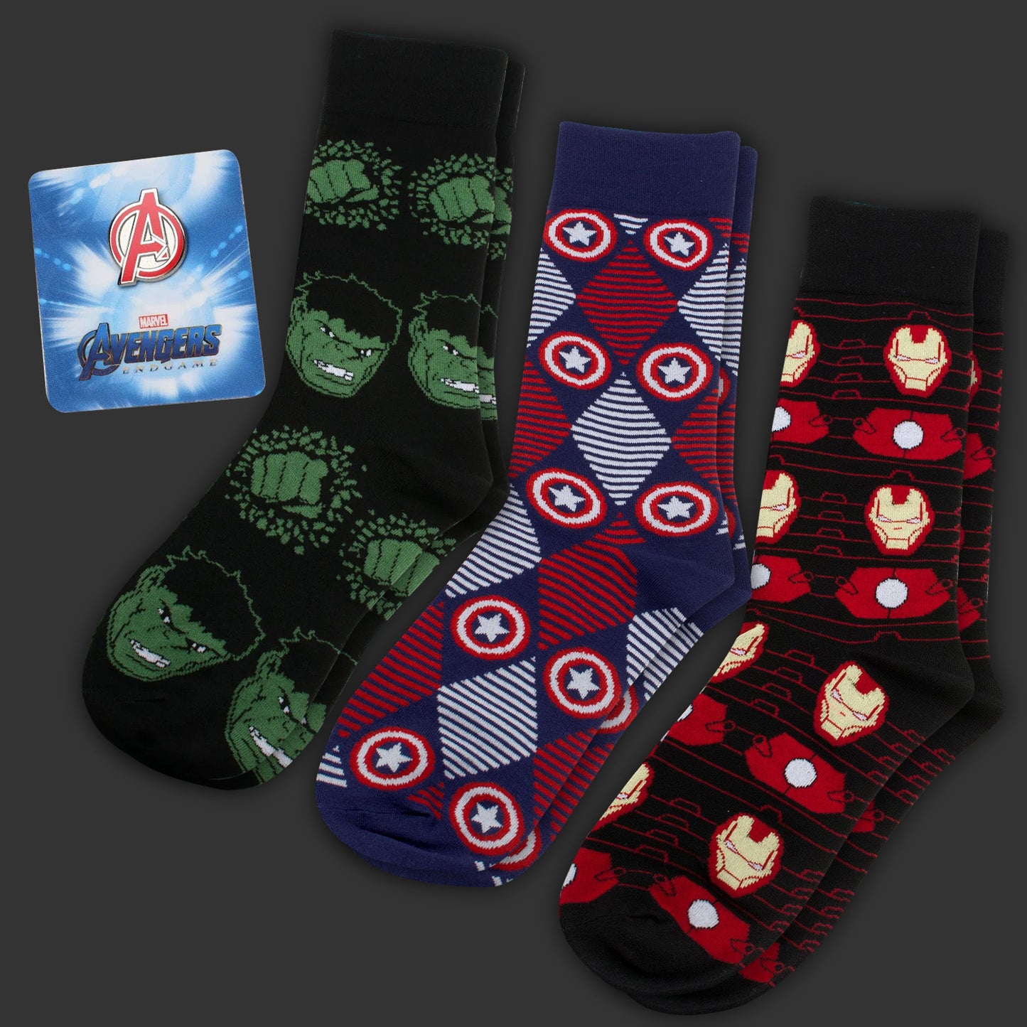 Three pairs of socks with superhero designs and an Avengers lapel pin on a dark background