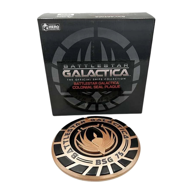 A bronze and black, round plaque, bearing the seal of the Battlestar Galactica. Behind the seal is a black box.