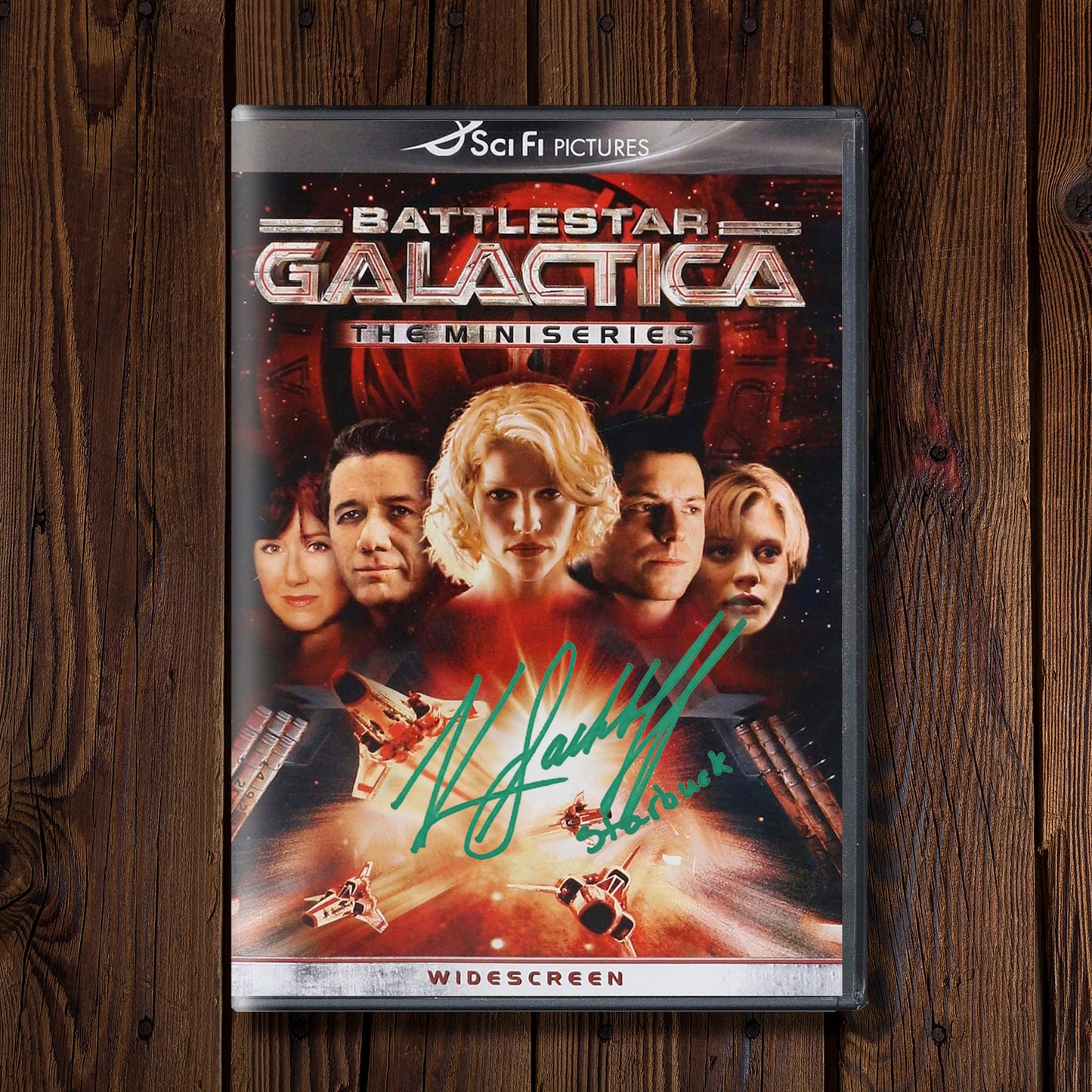 DVD cover of 'Battlestar Galactica' miniseries on a wooden surface. On the cover is Katee Sackhoff's autograph