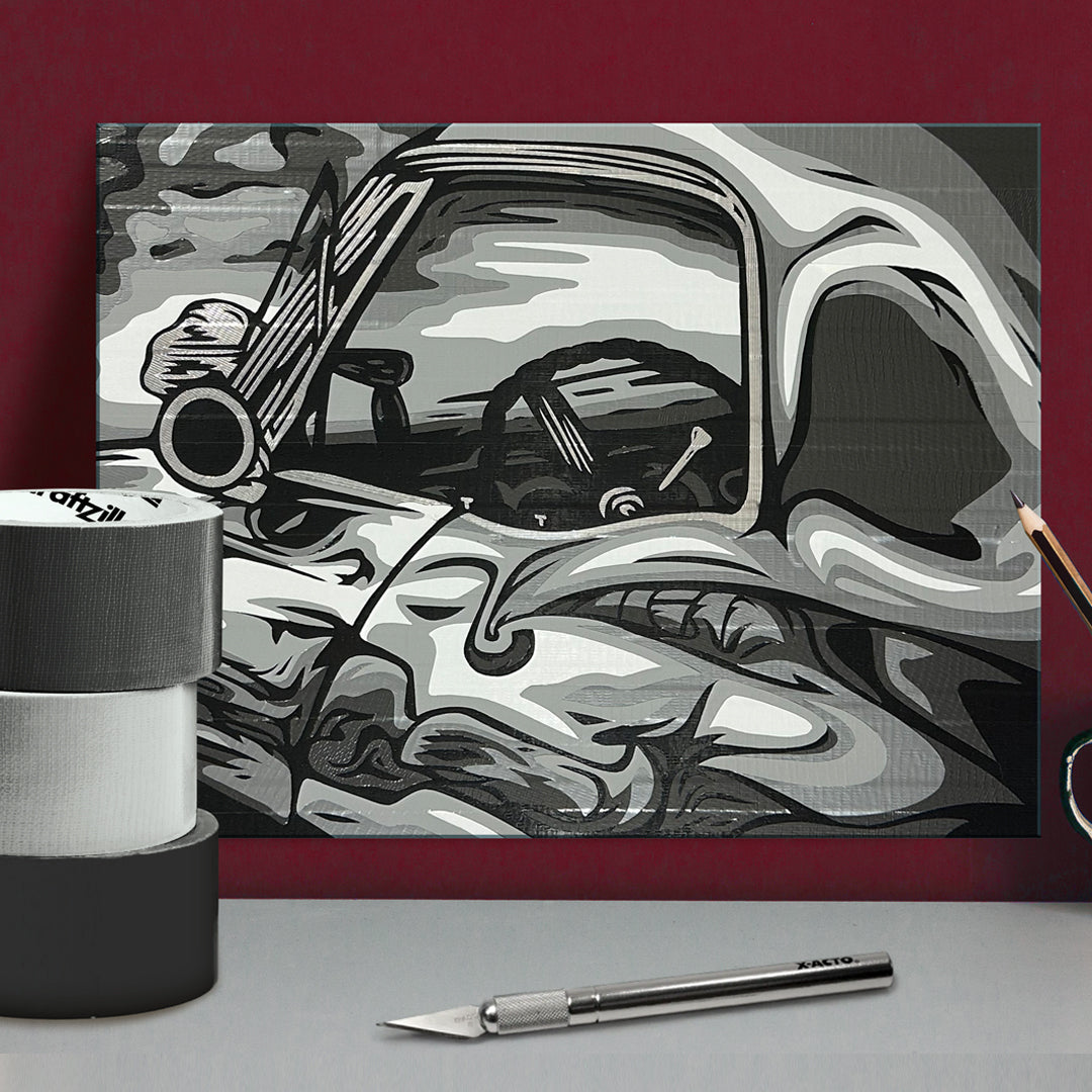 A black and white image of Baby, a 1967 Impala, created with multiple shades of duct tape. The piece is resting against a red background, with rolls of duct tape and an Xacto knife visible on a table below.