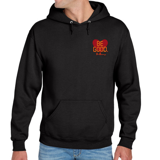 A model in a black hoodie against a white background. On the top left of the hoodie is a red heart. On top of the heart is "Be Good" in yellow text, stylized to look like text from old electronics.