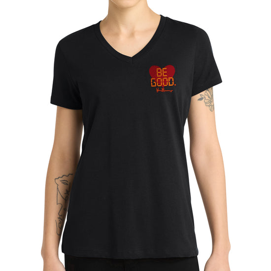 A model in a black tee shirt against a white background. On the top left of the shirt is a red heart. On top of the heart is "Be Good" in yellow text, stylized to look like text from old electronics.